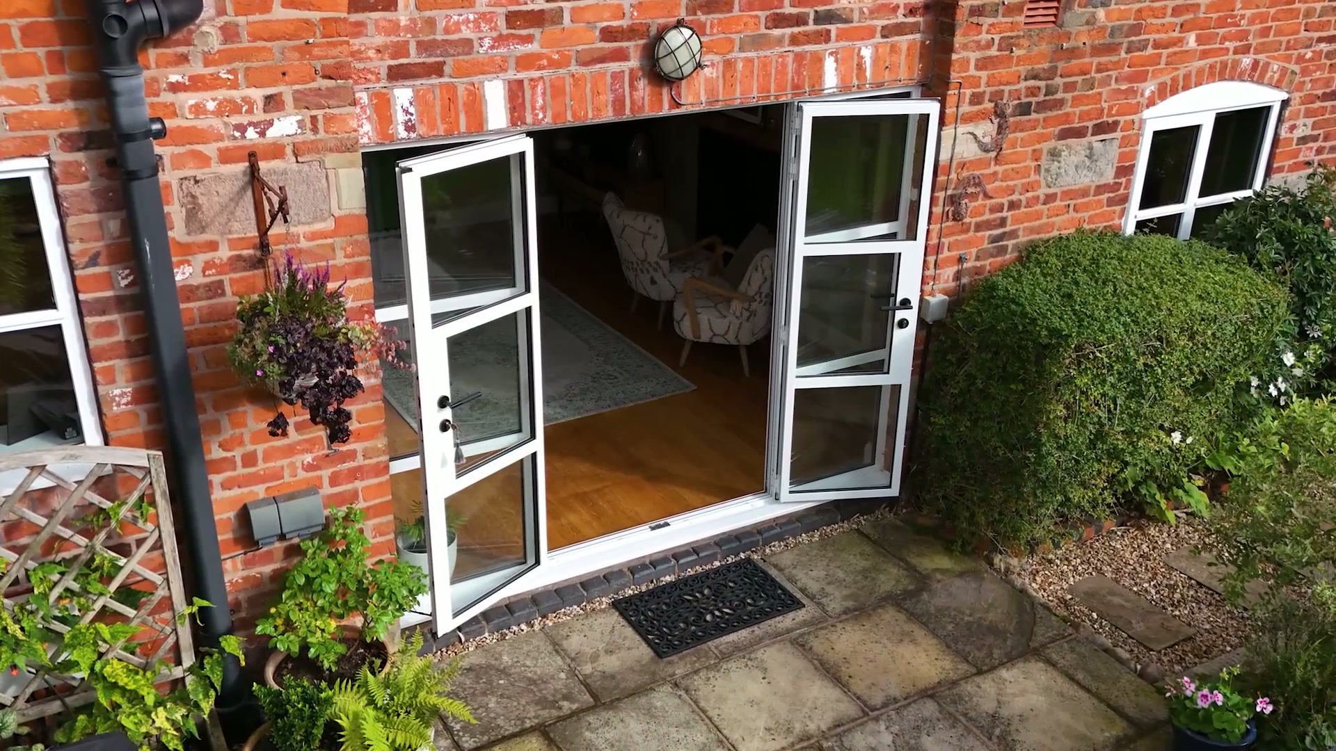 Aluminium French doors thrown open to the terrace, white frames against weathered brick