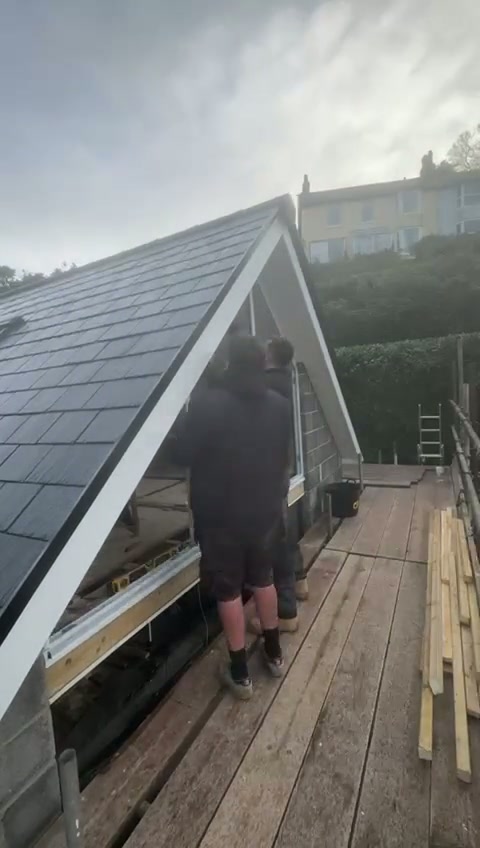 Two installers work the frame together, packing it off the structure so the aluminium carries no twist from the building.